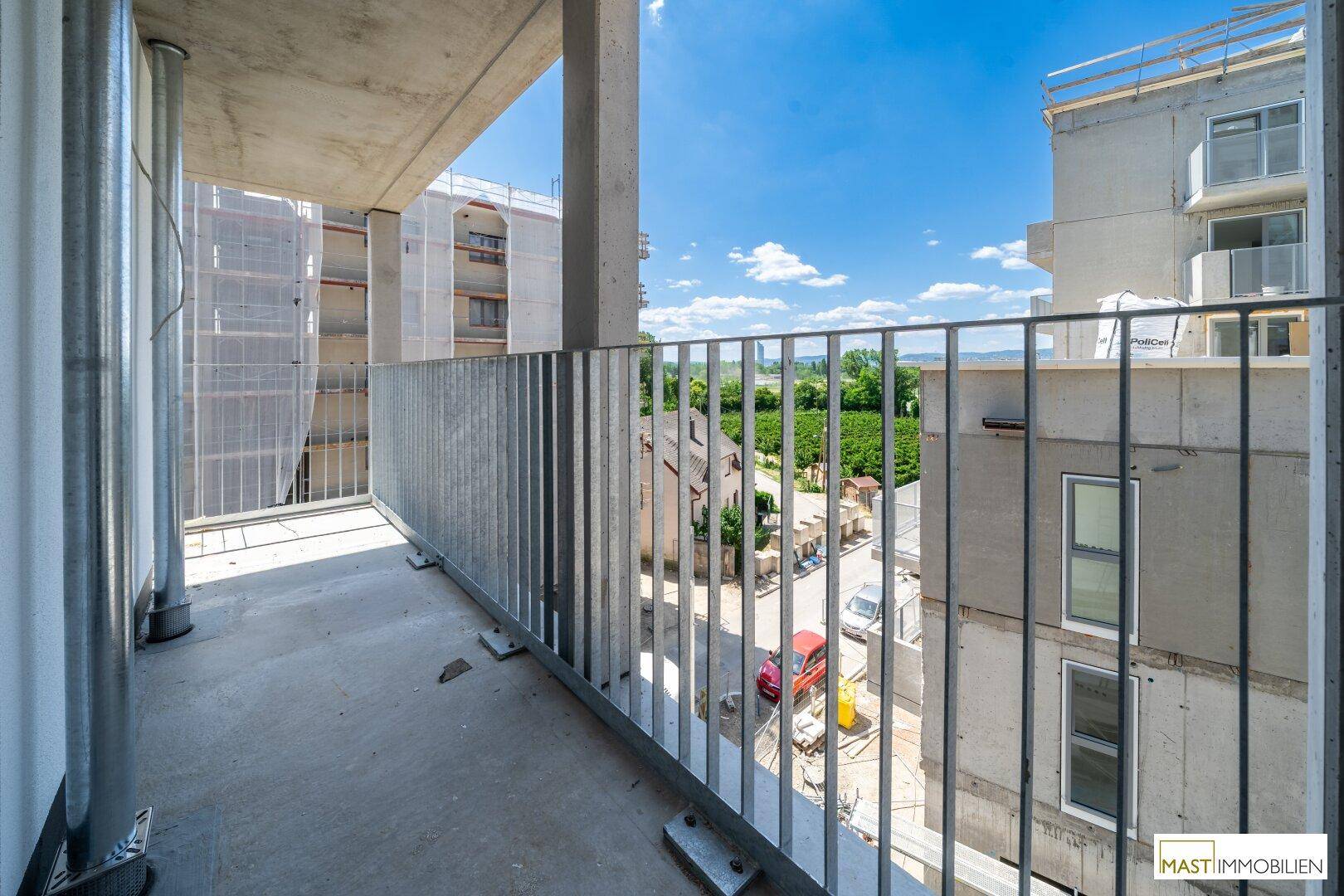 Balkon eines Neubaus mit Blick auf die Umgebung und entfernte Weinberge unter blauem Himmel.