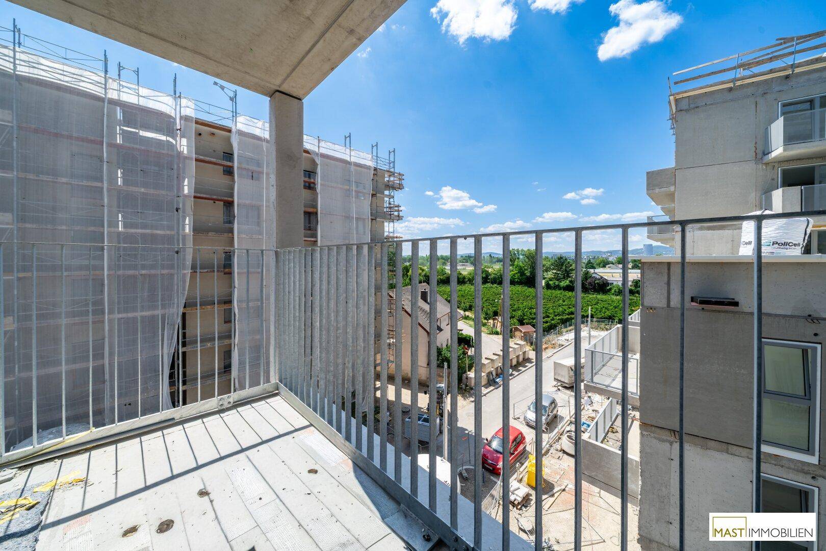 Balkon eines Neubaus mit weitem Blick über die Landschaft und angrenzende Gebäude.