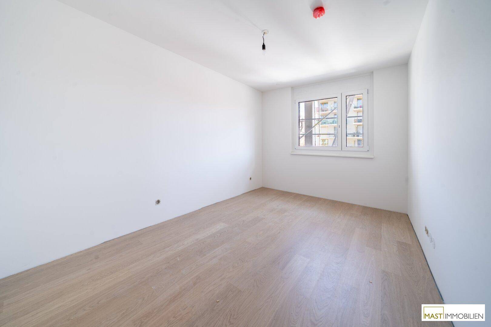 Leeres Zimmer mit hellem Laminatboden und Fenster, bereit für die individuelle Gestaltung.