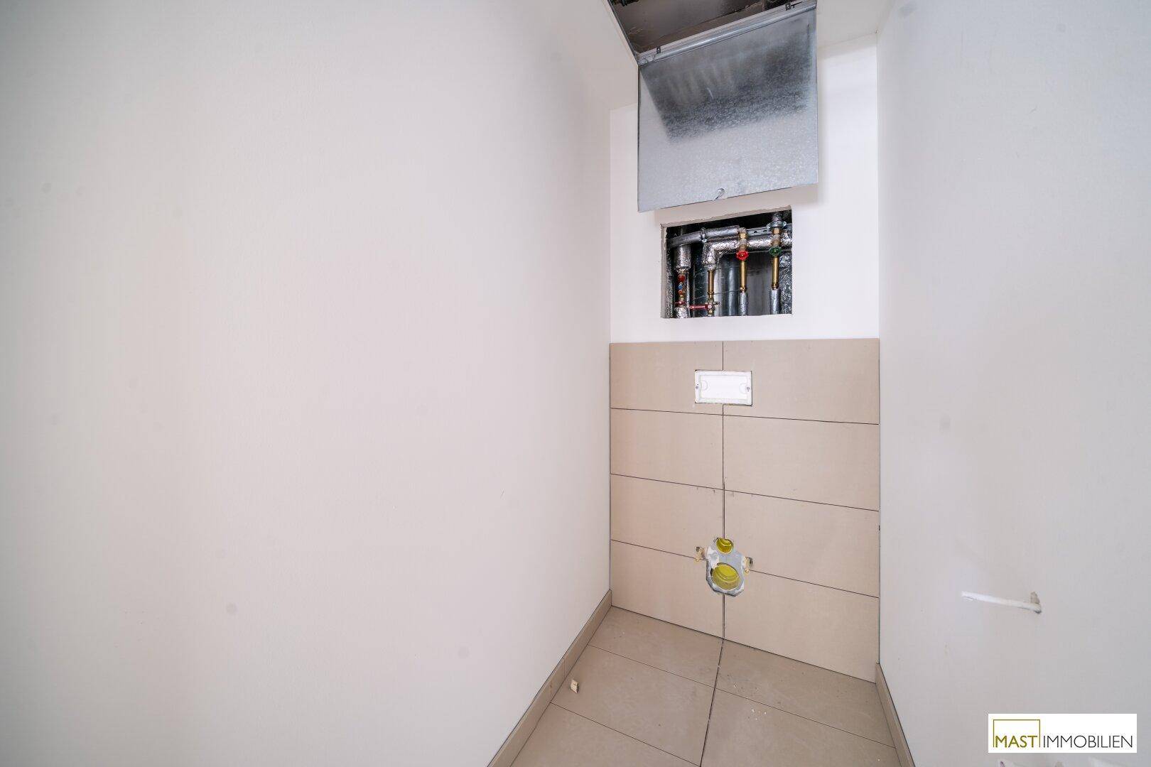 Kleines WC mit beigefarbenen Fliesen und Vorinstallation für ein wandhängendes WC.