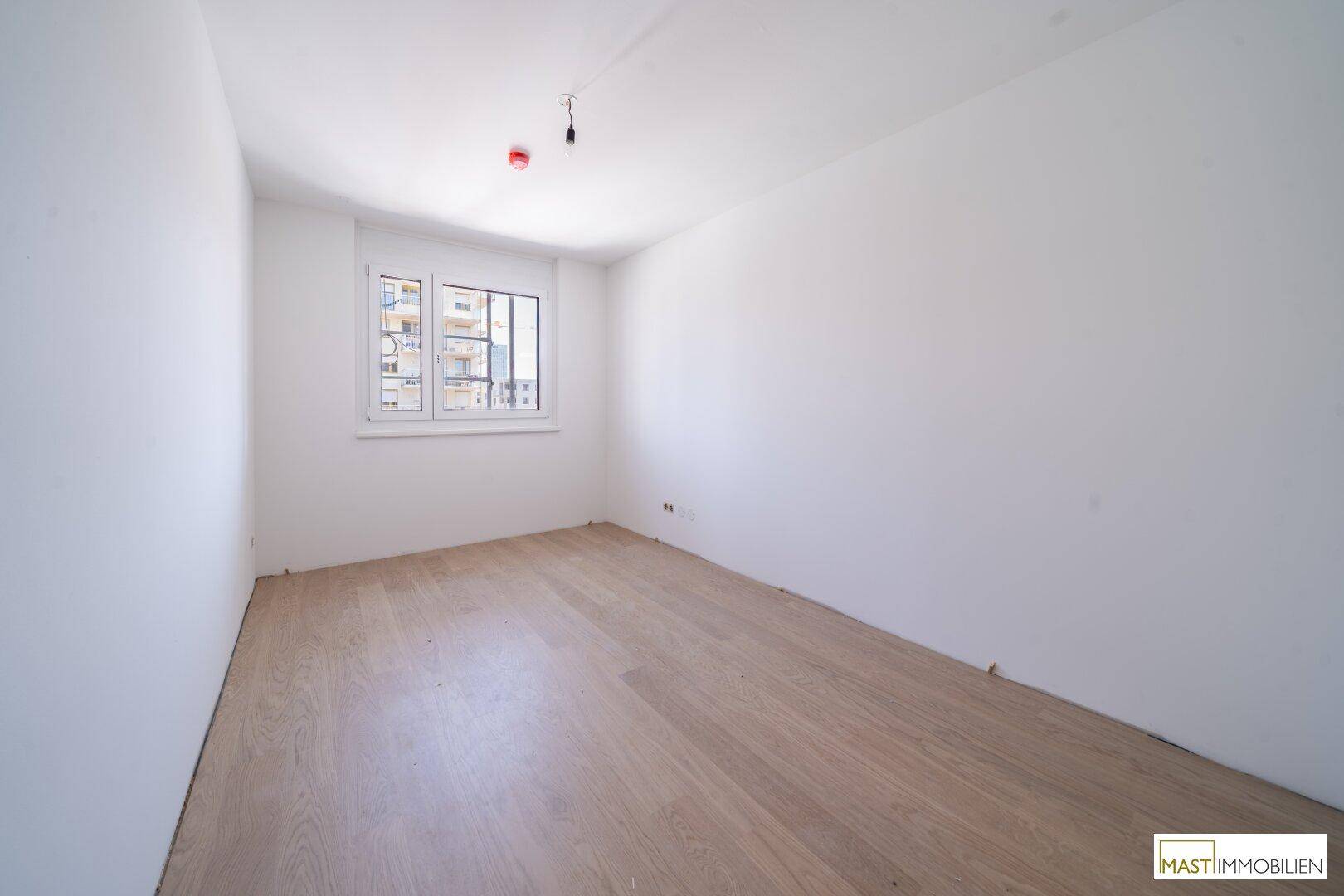 Helles Schlafzimmer mit neuem Laminatboden und Blick auf die umliegenden Gebäude.