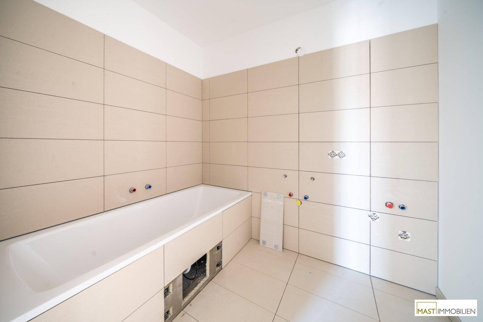 Badezimmer im Bau mit beigefarbenen Fliesen und eingebauter Badewanne, bereit zur Fertigstellung.