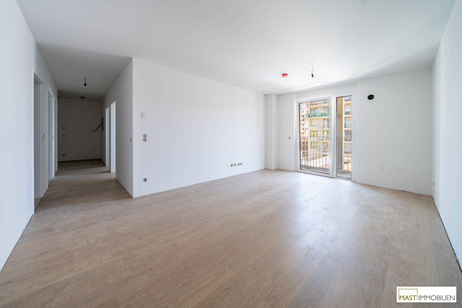 Geräumiges Wohnzimmer mit hellem Laminatboden und Zugang zu einem Balkon.