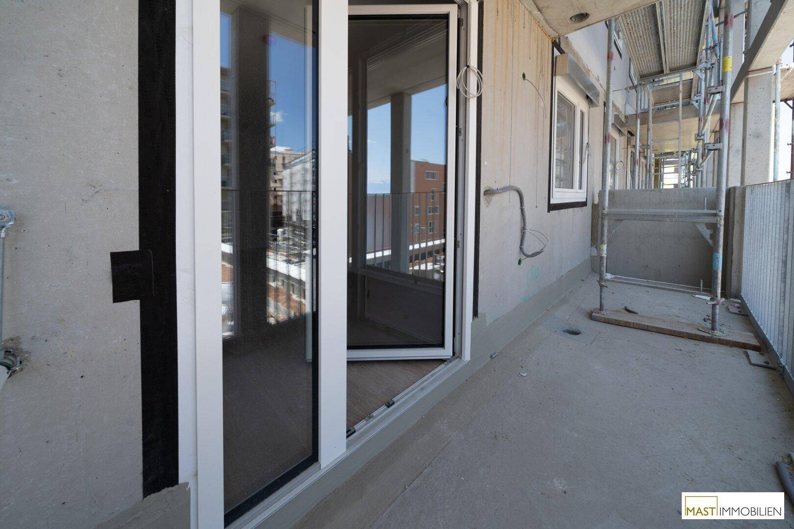 Balkon im Bau mit Zugang zum Innenraum und Blick auf die Baustelle und Nachbargebäude.