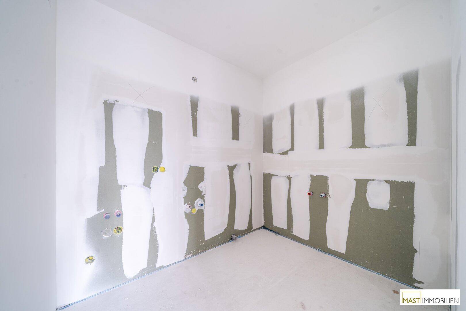 Ecke eines Raumes im Rohbau mit vorbereiteten Wänden und sichtbaren Installationsanschlüssen.