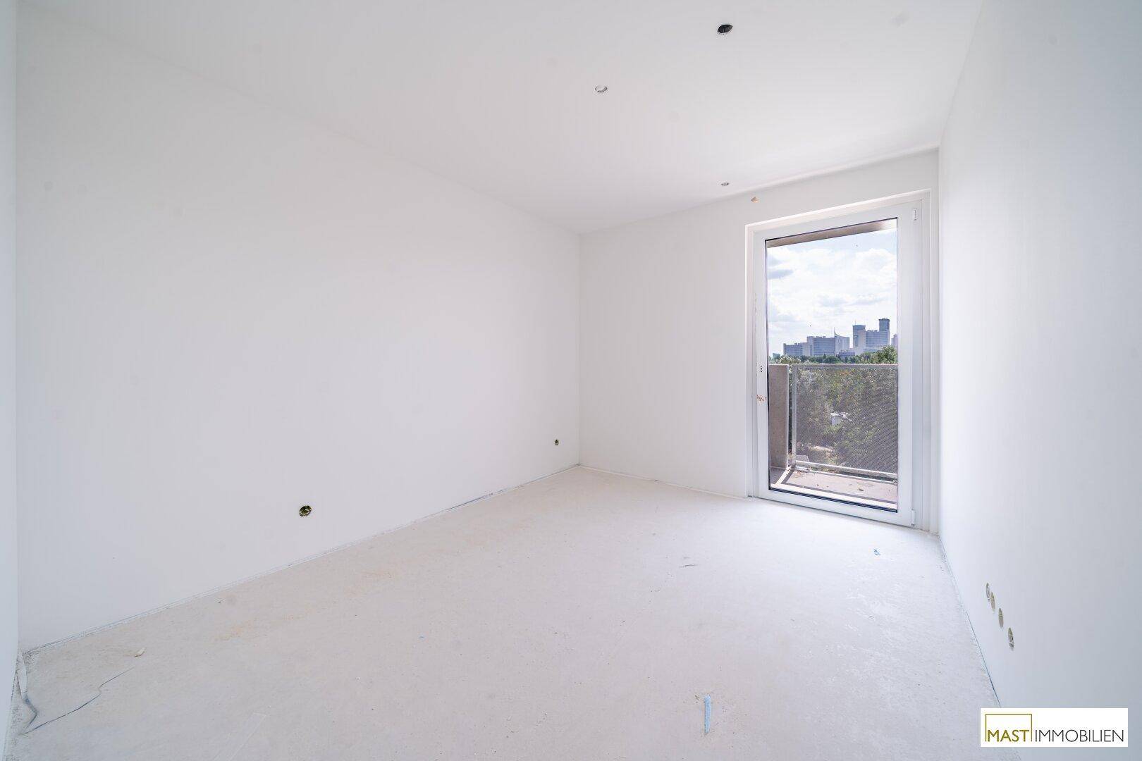 Helles Schlafzimmer im Rohbau mit weiß gestrichenen Wänden und Balkonzugang.