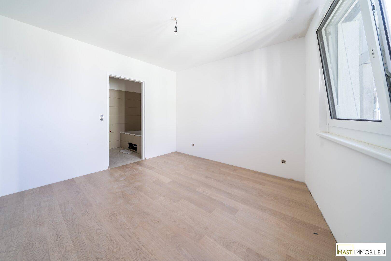Unmöbliertes Zimmer mit Holzfußboden und Zugang zu einem gefliesten Badezimmer.