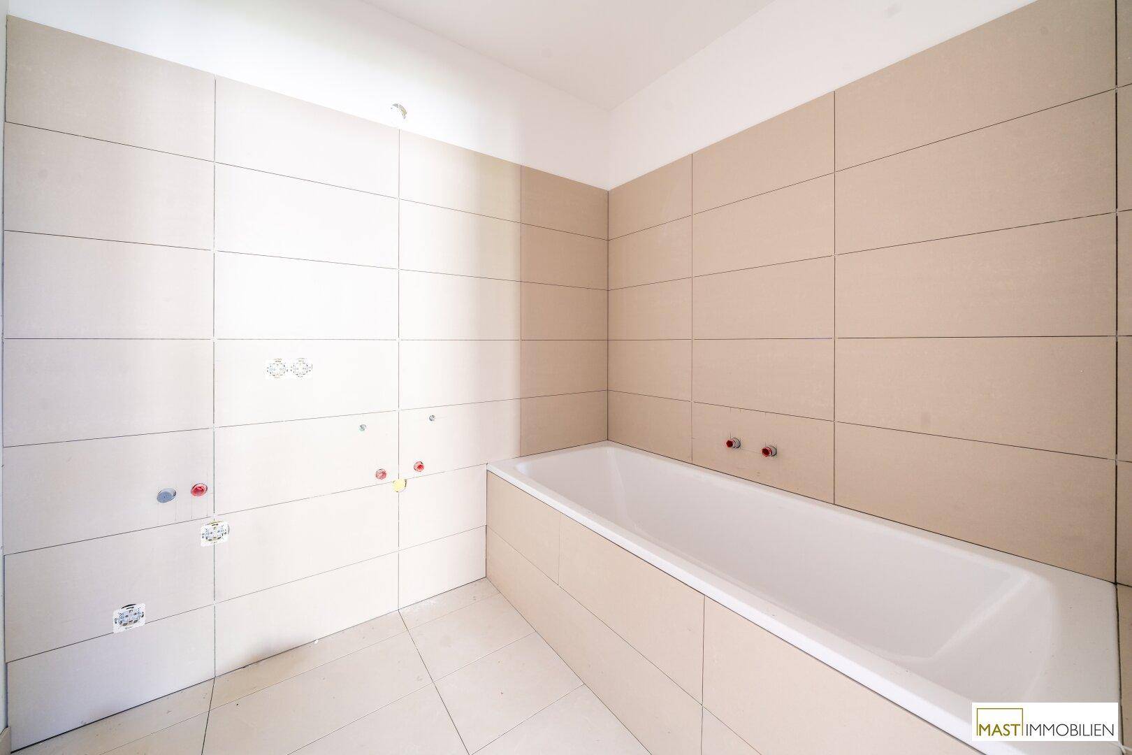 Badezimmer im Bauzustand mit beigefarbenen Fliesen an Wänden und Boden sowie einer eingebauten Badewanne.
