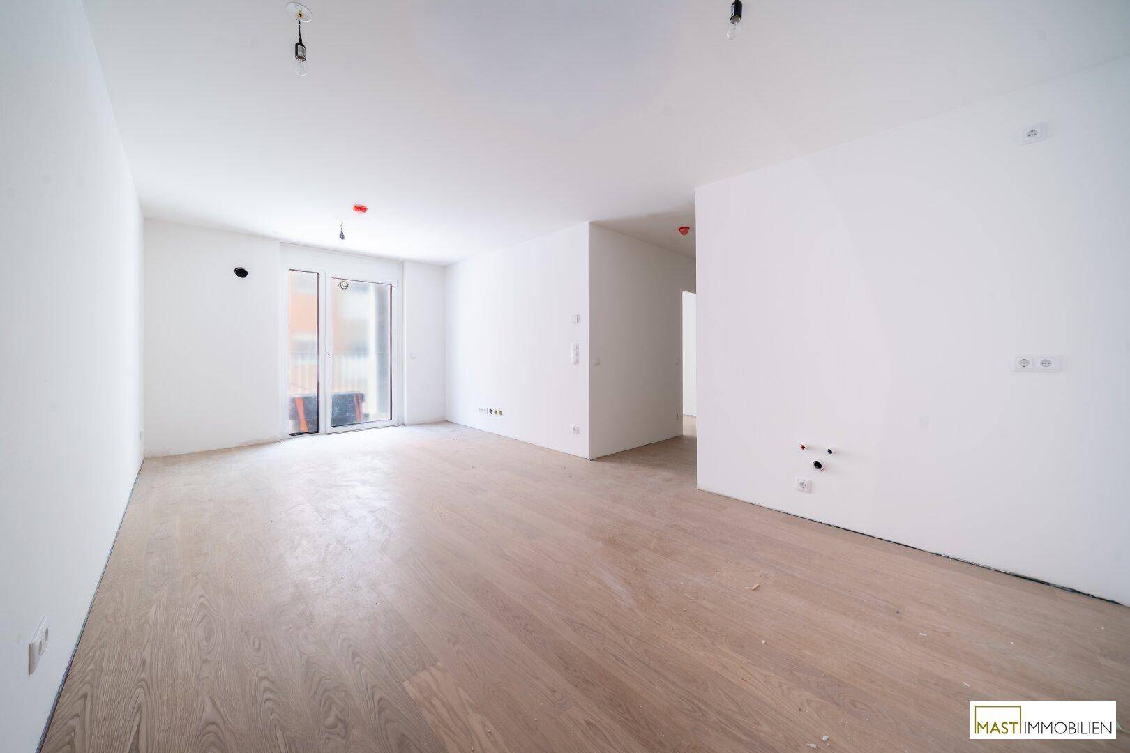 Helles, leeres Wohnzimmer mit neuem Laminatboden und Zugang zu einem Balkon.