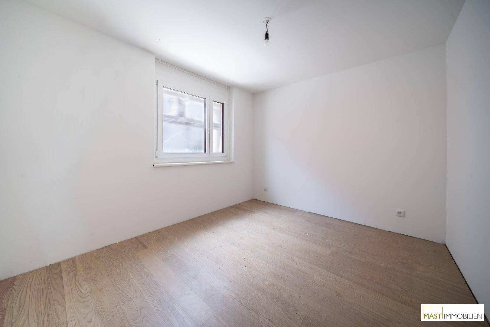 Unmöbliertes Zimmer mit Laminatboden und einem Fenster, ideal als Schlaf- oder Arbeitszimmer.