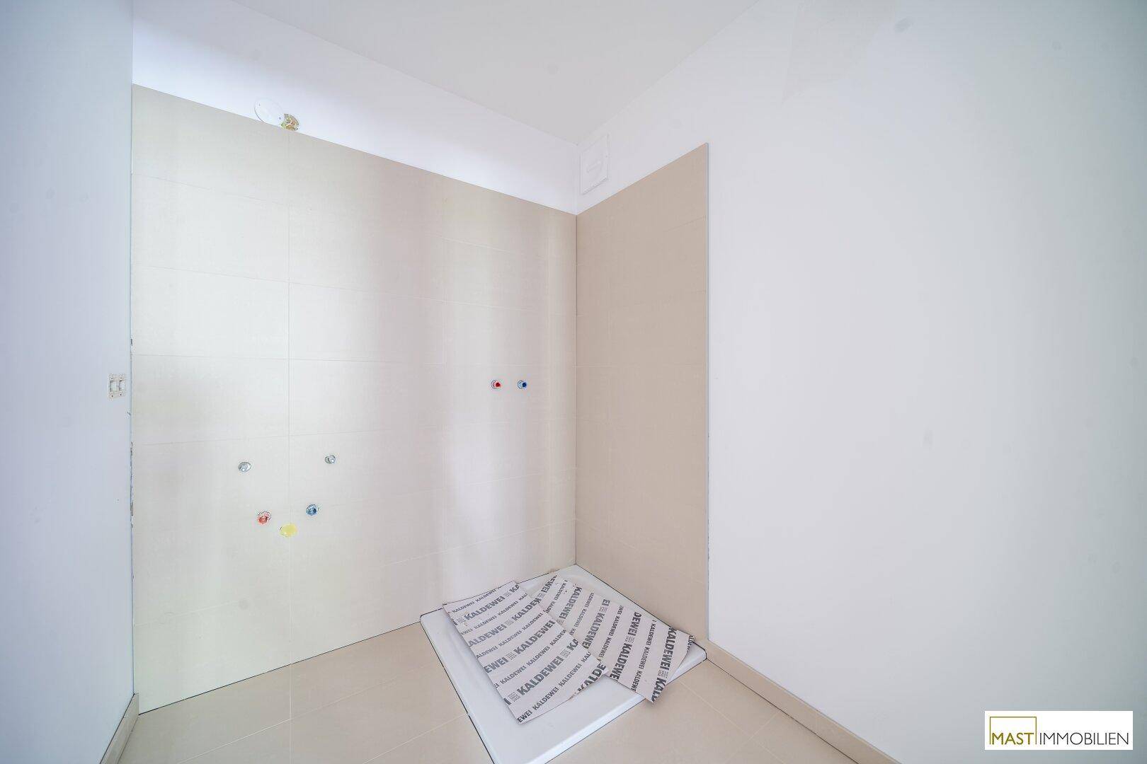 Badezimmer im Bau mit gefliesten Wänden und vorbereiteten Anschlüssen für Sanitärinstallationen.