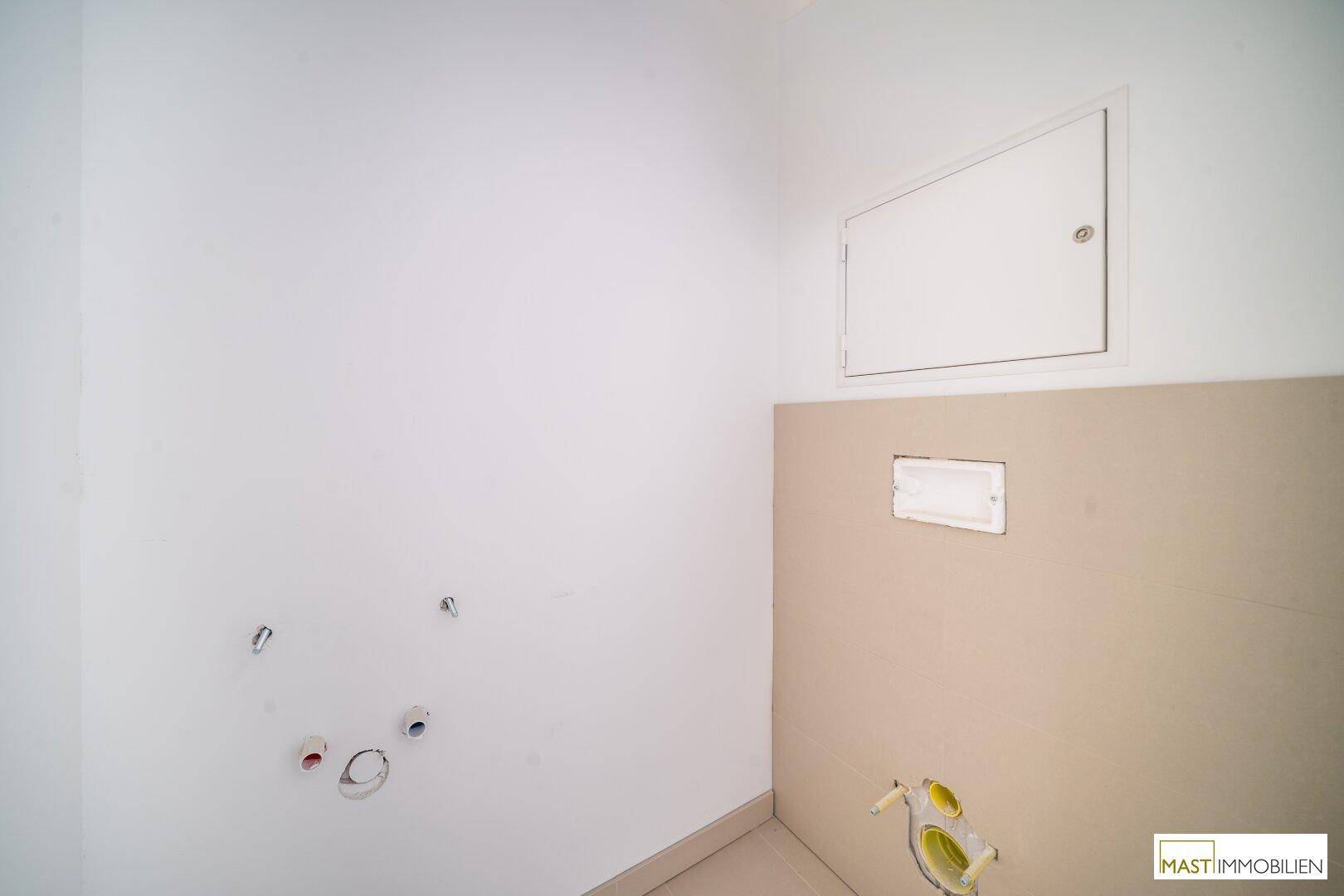 Kleiner WC-Raum mit vorbereiteten Anschlüssen für eine Wandtoilette und Zugangsklappe.