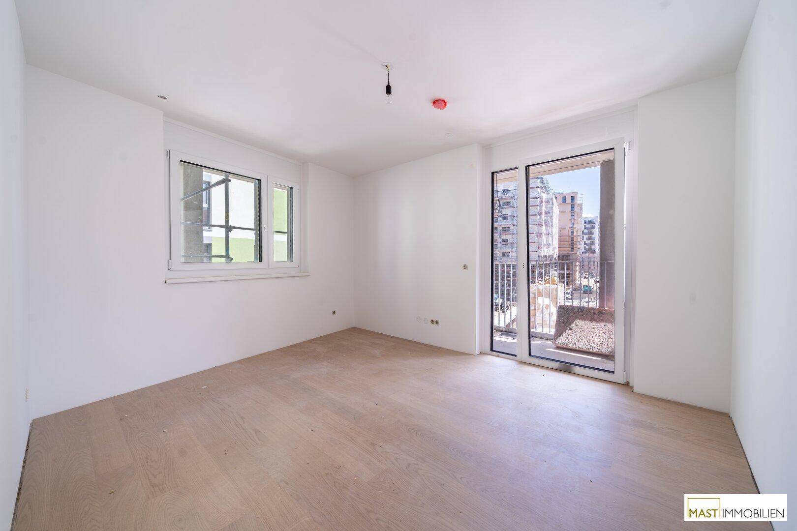 Helles, leeres Zimmer mit Parkettboden und Zugang zu einem Balkon, bereit für die Einrichtung.