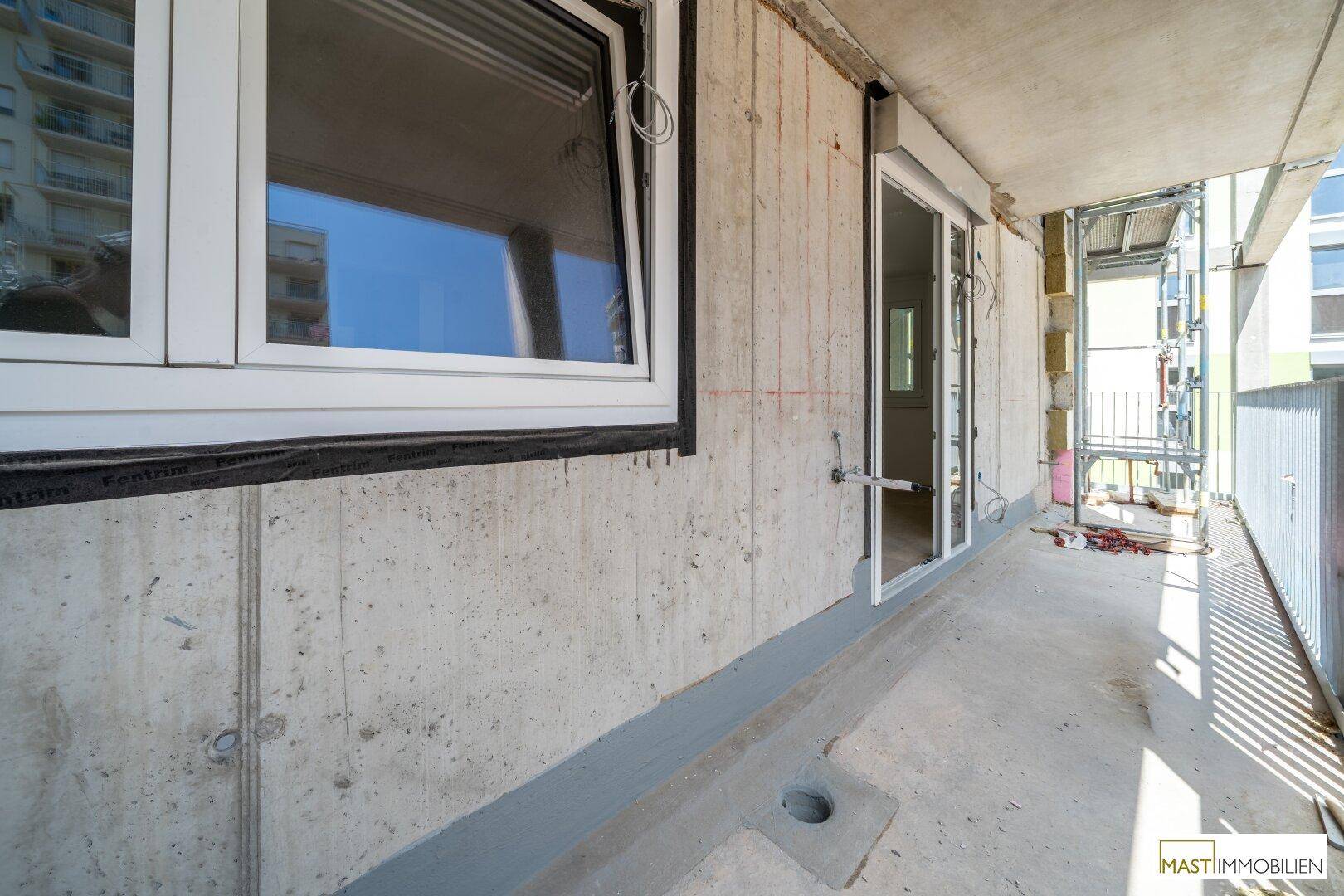 Balkon mit Betonwand und Fenster, das den Blick auf die Baustelle freigibt.