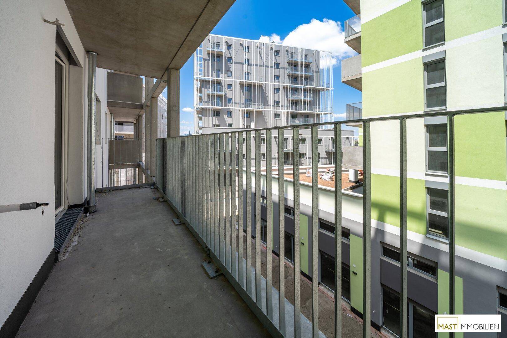 Geräumiger Balkon mit Metallgeländer und weitem Blick auf die moderne Architektur der Umgebung.