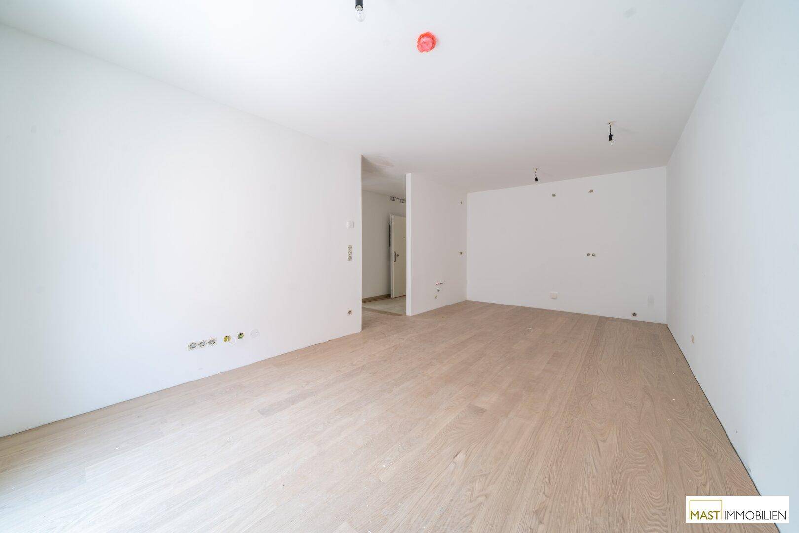 Geräumiger, leerer Raum mit hellen Wänden und neuem Holzboden, bereit für die individuelle Gestaltung.