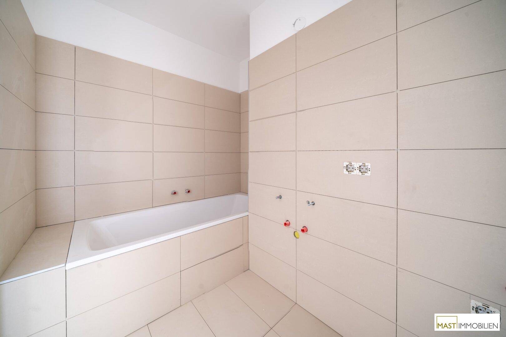 Modernes Badezimmer mit beigefarbenen Fliesen und einer eingebauten Badewanne, noch ohne Armaturen.