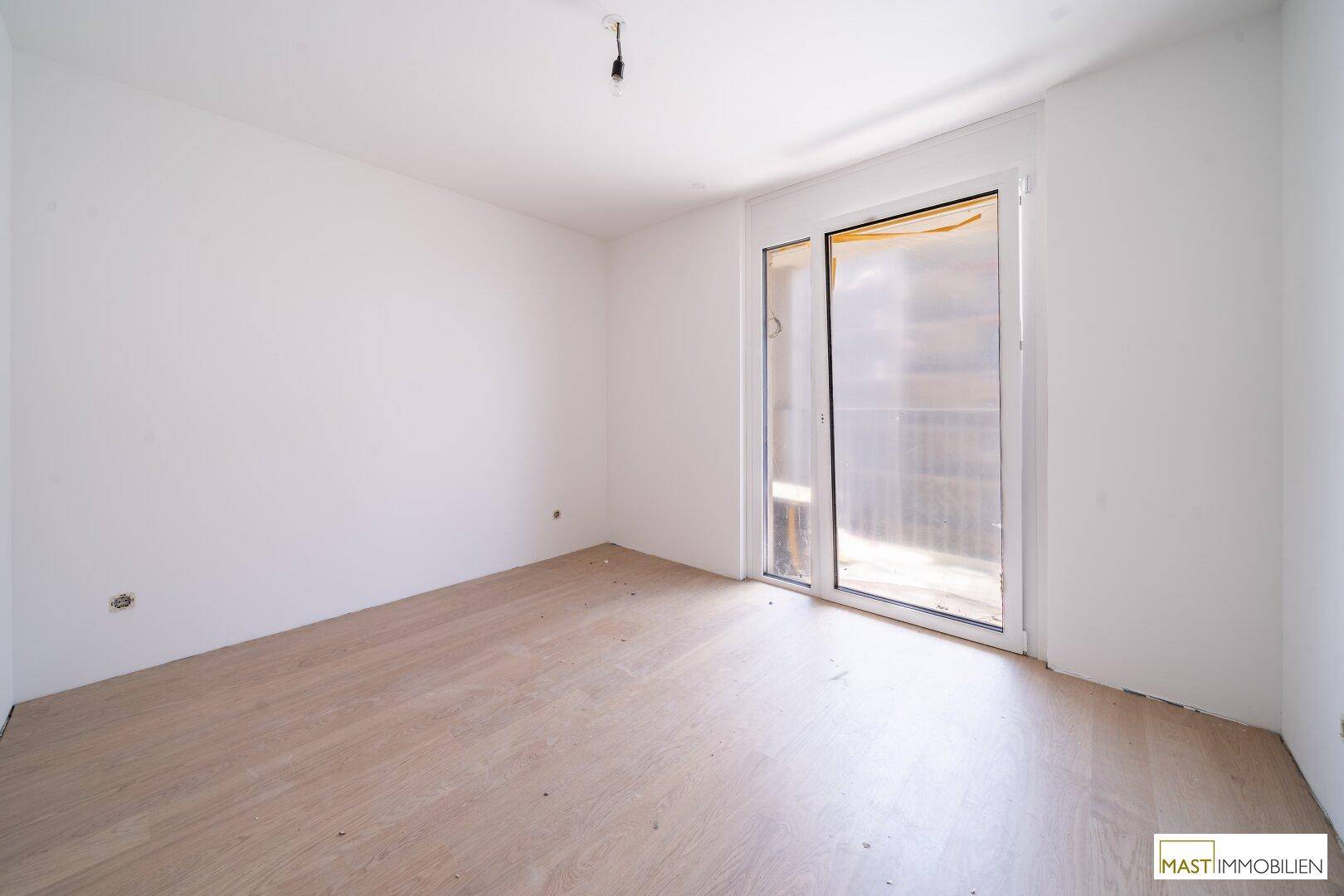 Unmöbliertes Zimmer mit Parkettboden und Schiebetür zum Balkon, ideal als Schlafzimmer.
