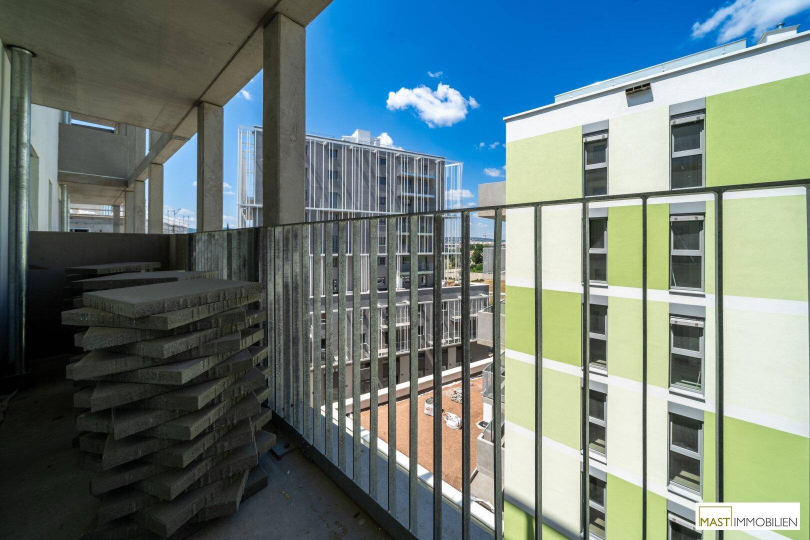 Balkon im Bau mit Blick auf angrenzende Neubauten und den blauen Himmel.