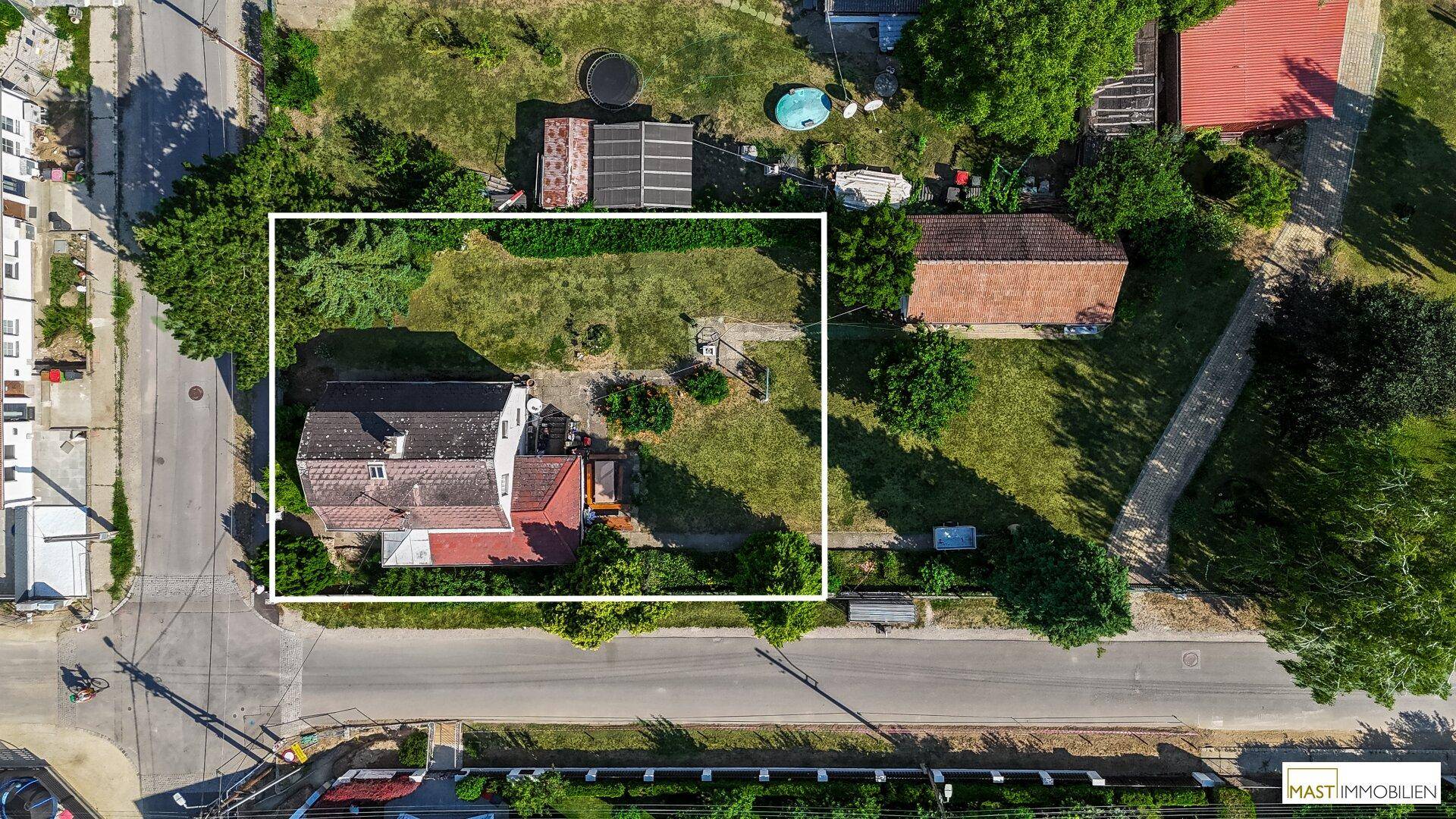 Luftaufnahme eines Einfamilienhauses mit großem Garten, Zufahrt und umliegender grüner Landschaft.