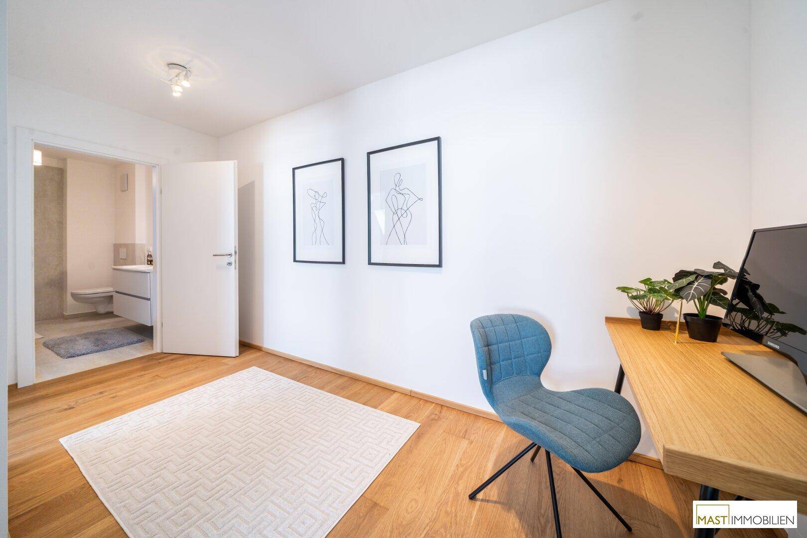 Helles Zimmer mit Schreibtisch, Holzboden und direktem Zugang zu einem Badezimmer.