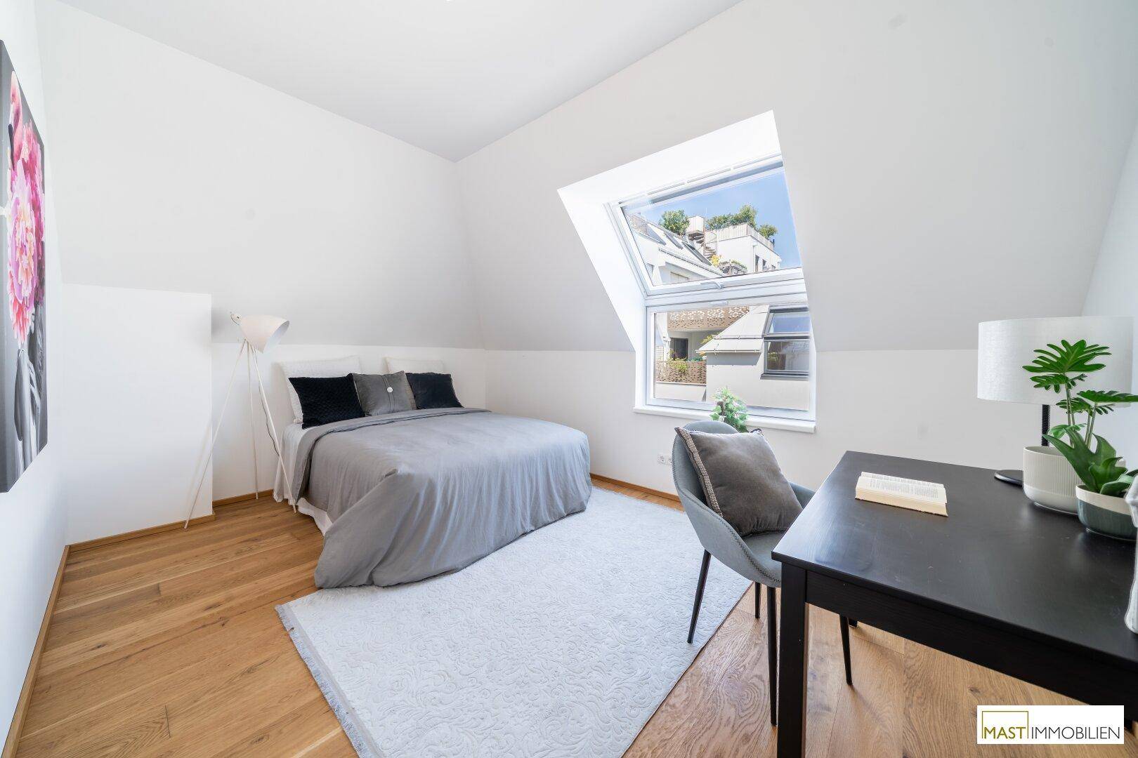 Helles Schlafzimmer im Dachgeschoss mit Holzboden, Schreibtisch und großem Dachfenster.