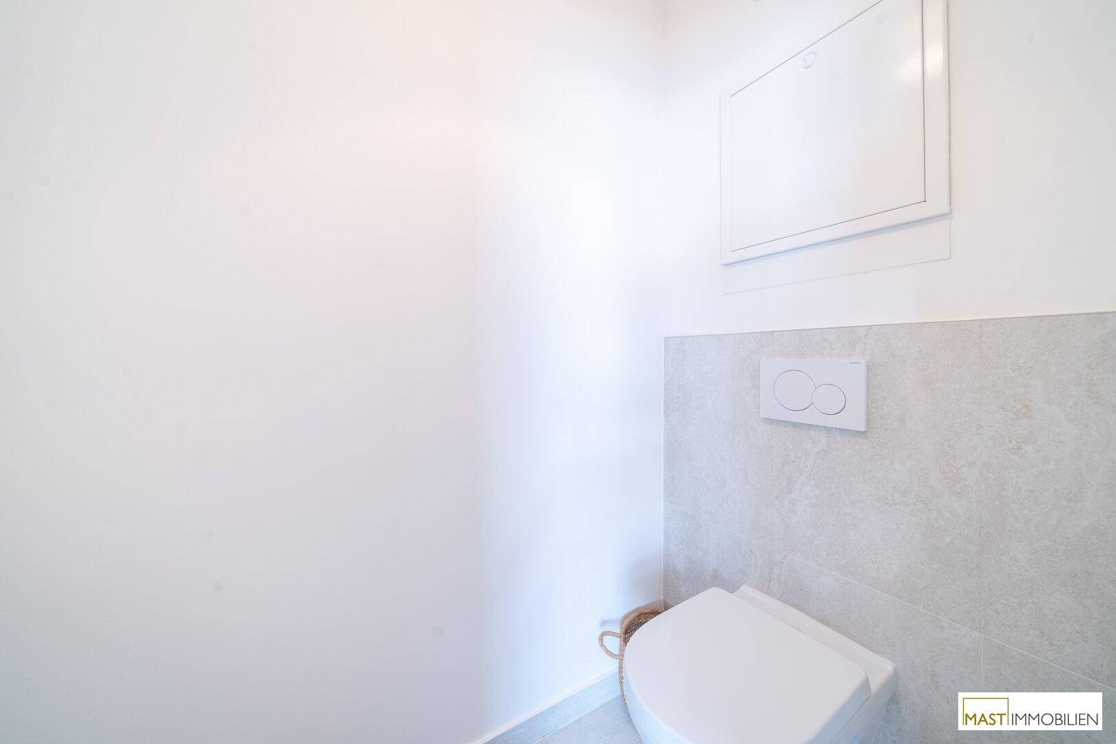 Separates WC mit wandhängender Toilette und modernen, hellgrauen Bodenfliesen.
