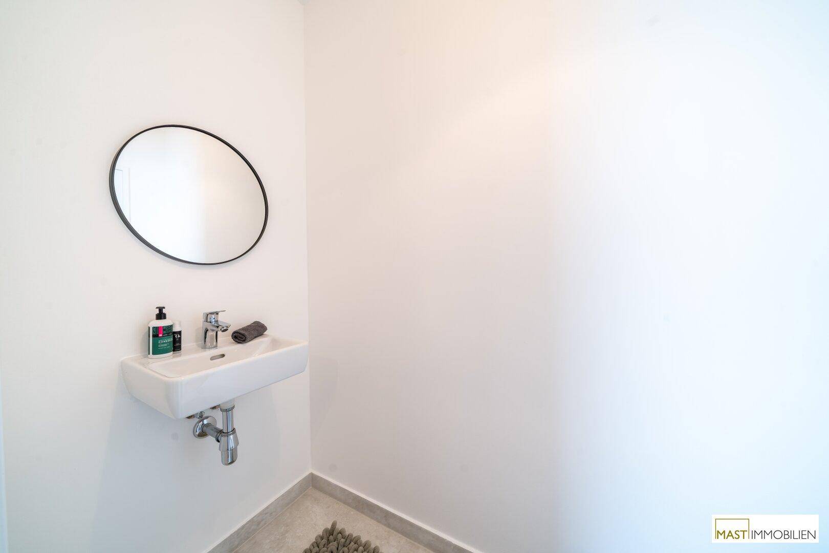 Kleines Gäste-WC mit modernem Waschbecken, rundem Spiegel und hellen Fliesen.