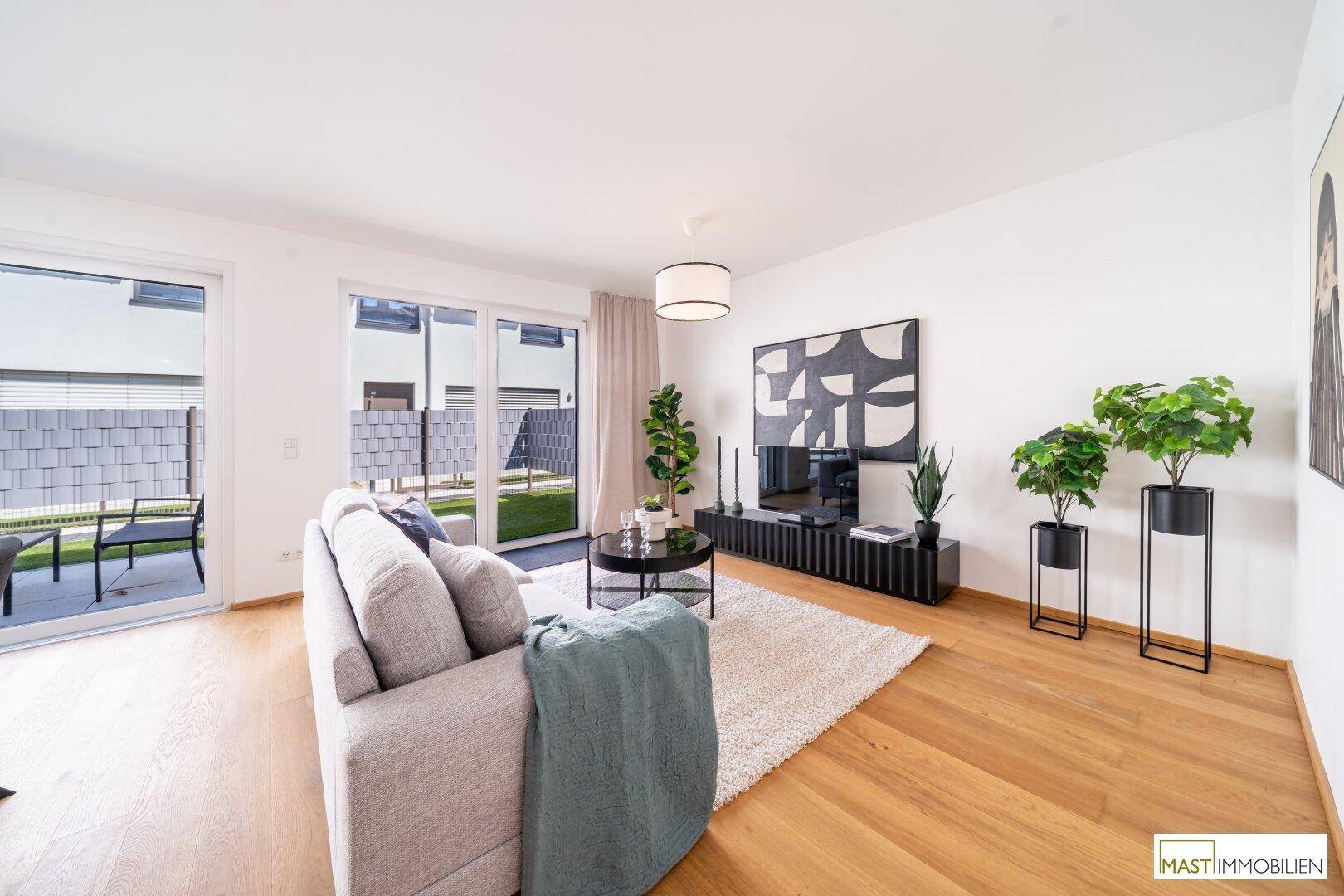 Gemütliches Wohnzimmer mit Sofa, Fernseher und Zugang zur Terrasse durch große Schiebetüren.