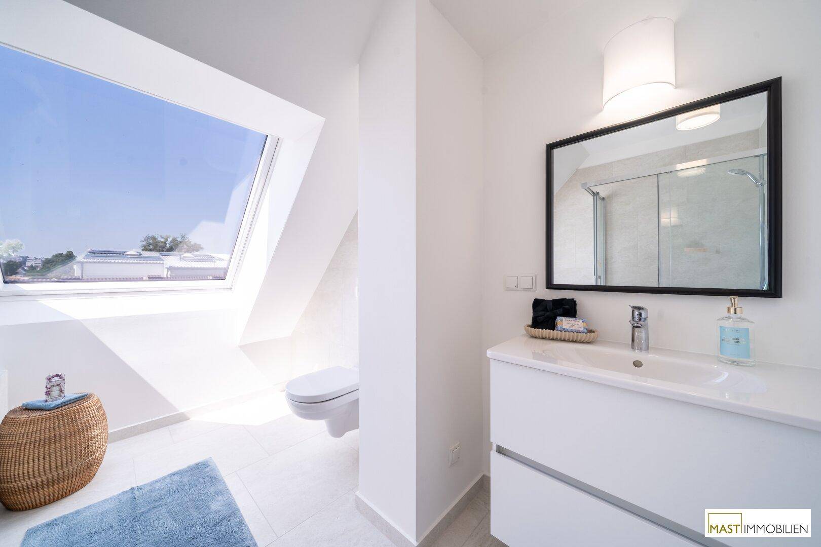 Modernes Badezimmer mit Waschtisch, Toilette und großem Dachfenster für Tageslicht.