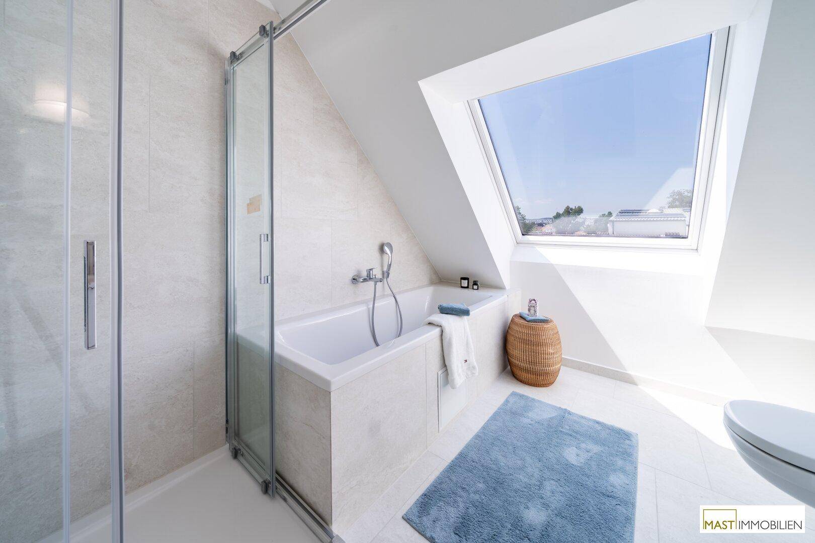 Helles Badezimmer mit Badewanne, Duschkabine und großem Dachfenster.