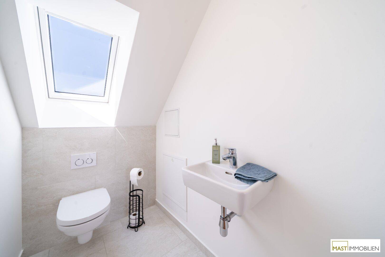 Separates Gäste-WC mit Waschtisch, wandhängender Toilette und Dachfenster.