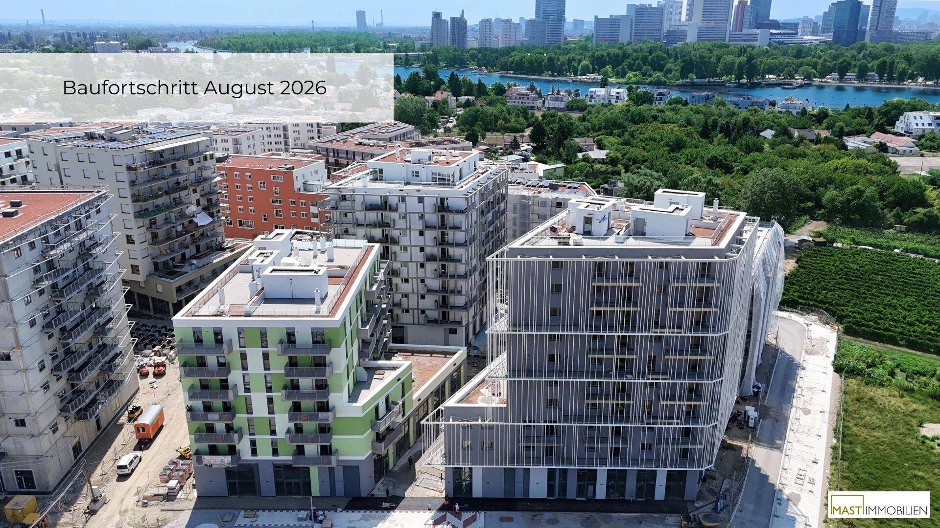 Luftaufnahme des Baufortschritts im August 2026 mit modernen Gebäuden und Blick auf die Stadt und den Fluss.
