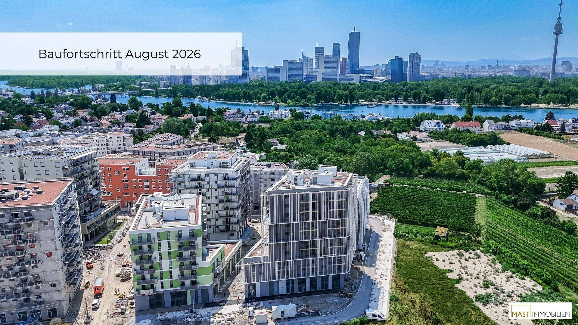Weitläufige Luftansicht der Neubauten, umgeben von Grünflächen und einem Fluss mit Stadtblick.