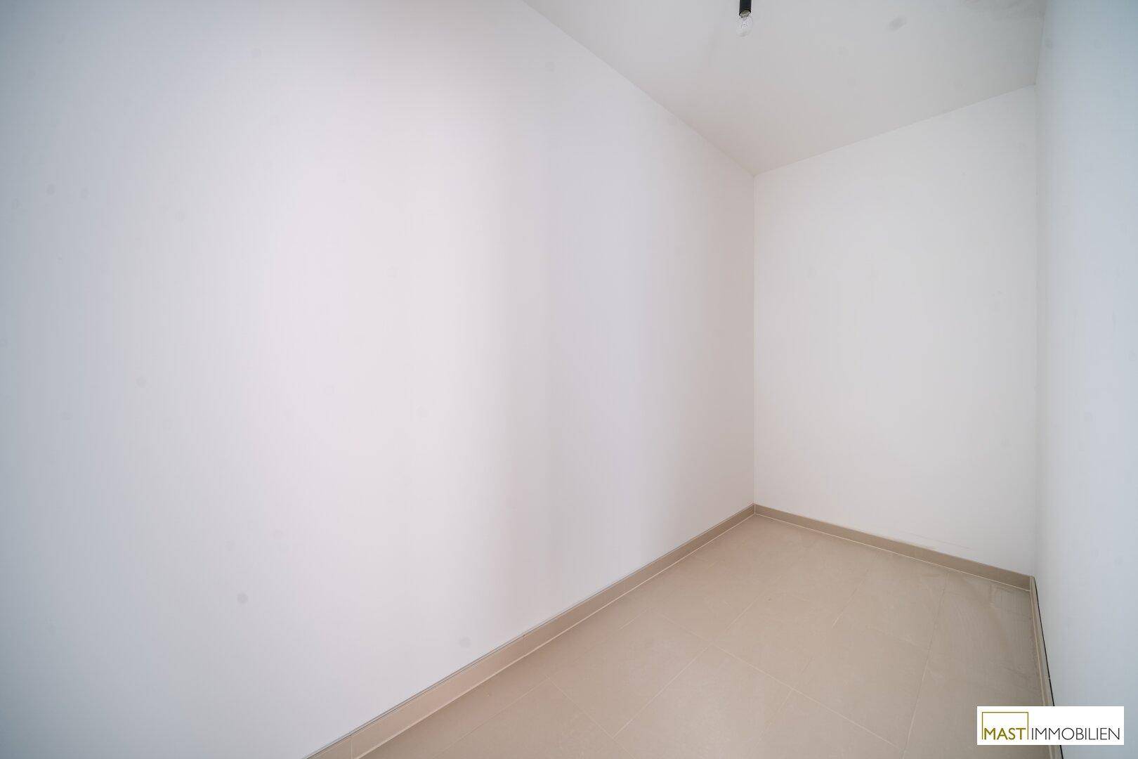 Leerer Raum mit hellen Fliesen und weißen Wänden, vielseitig nutzbar in einem Neubau.
