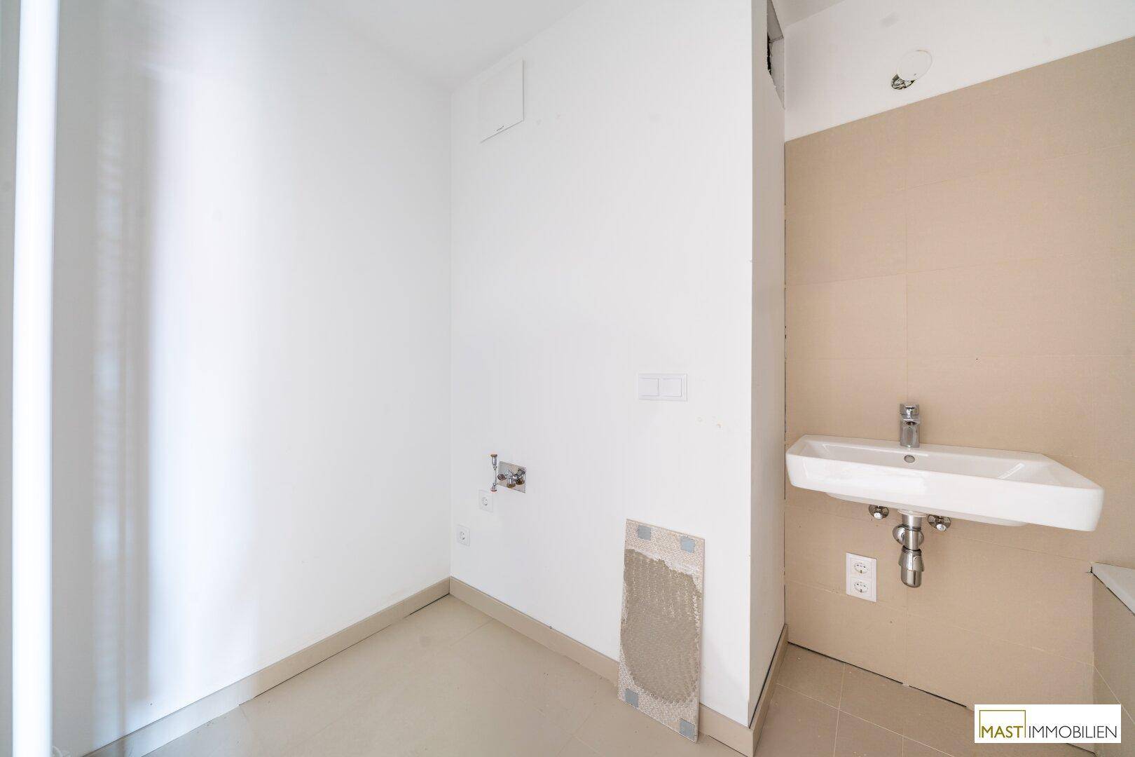 Unfertiges Badezimmer mit Waschbecken und vorbereiteten Anschlüssen für weitere Sanitärobjekte.