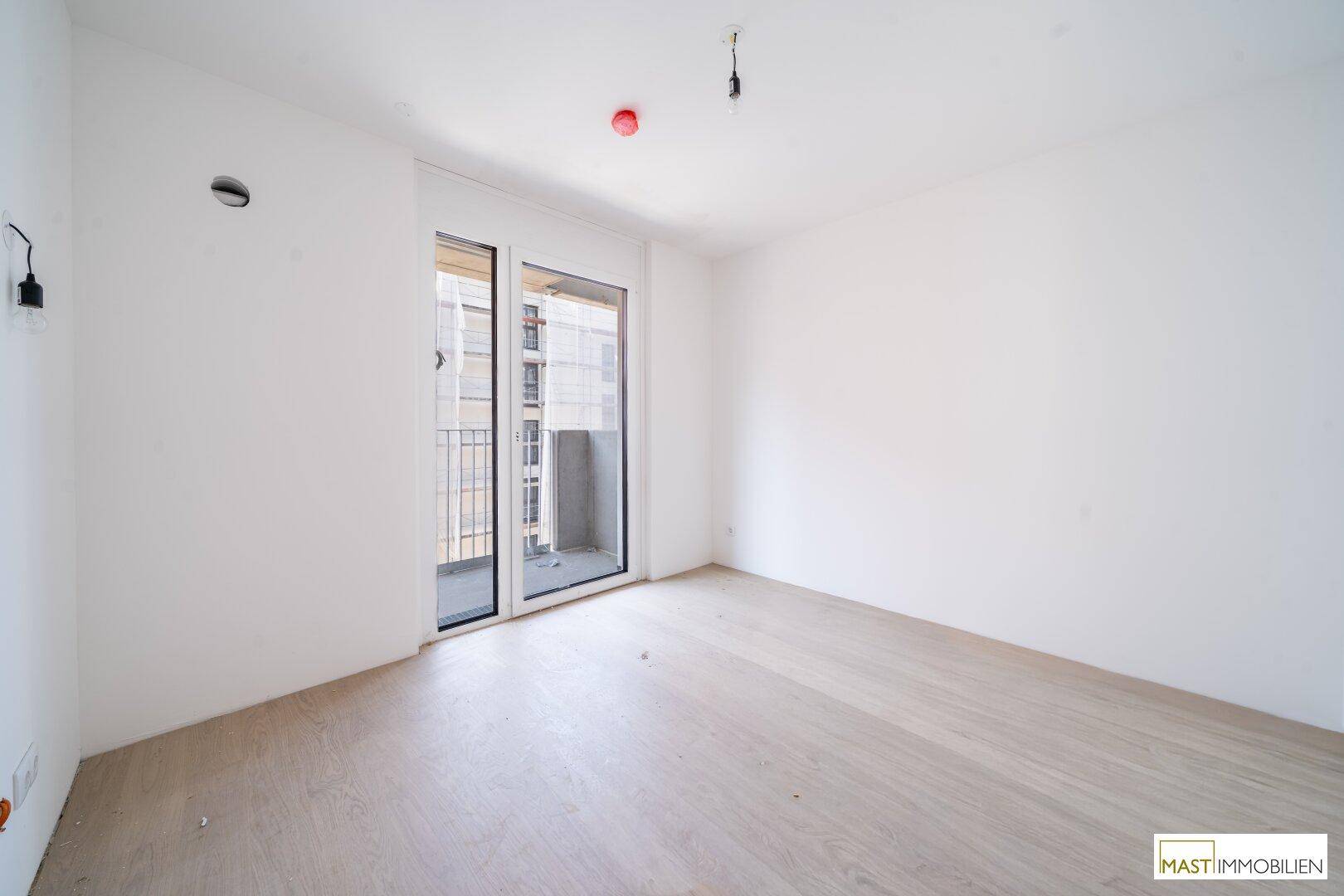 Helles Schlafzimmer mit Zugang zu einem Balkon und Blick auf die umliegenden Gebäude.