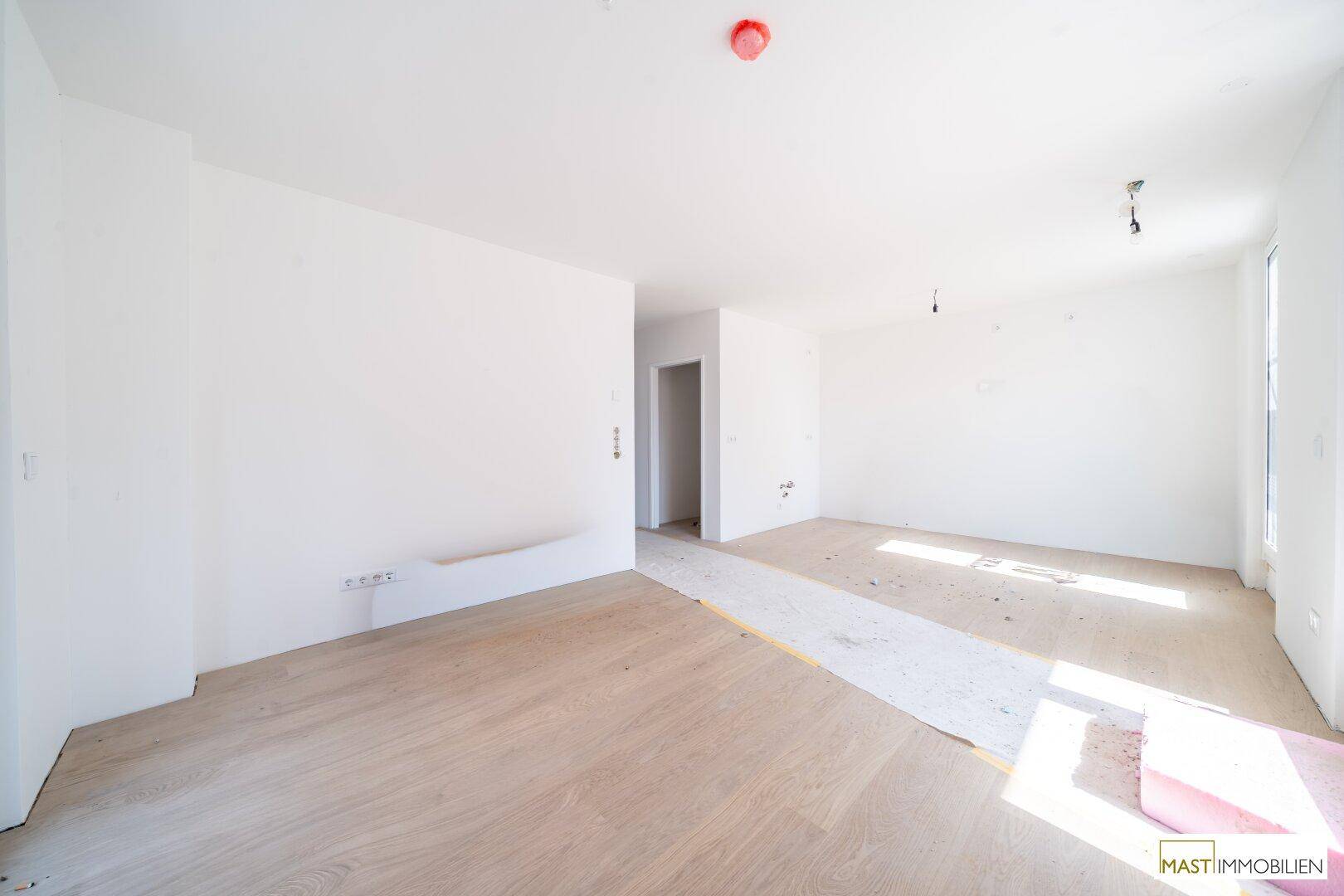 Geräumiger, unfertiger Raum mit hellem Boden und viel Tageslicht, bereit für den Ausbau.