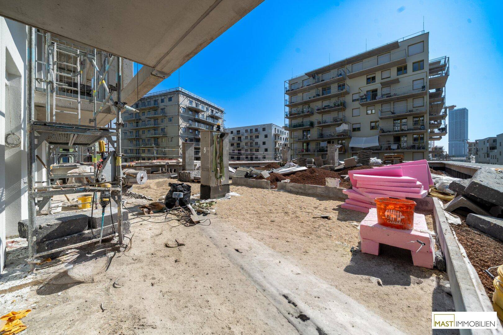 Weitläufige Baustelle mit mehreren im Bau befindlichen Wohngebäuden unter blauem Himmel.
