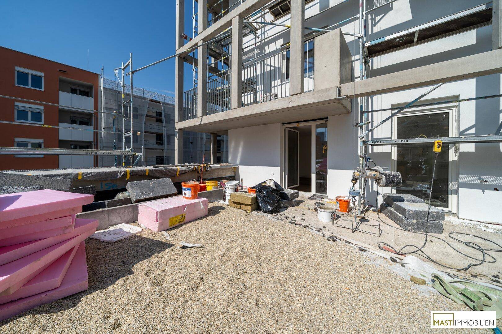 Baustellenbereich im Freien neben dem Neubau mit Baumaterialien und Gerüst.