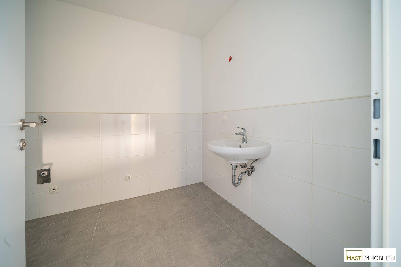 Modernes Badezimmer mit Waschbecken und Platz für eine Waschmaschine, hell gefliest.