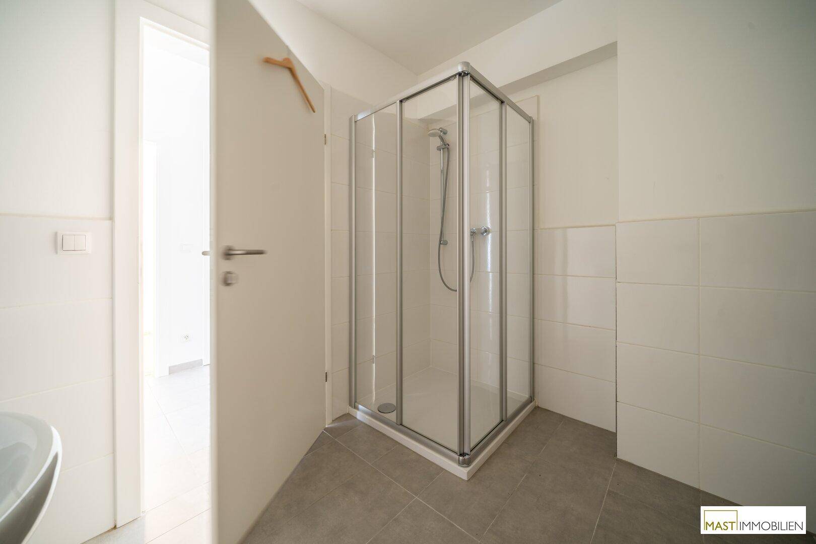Modernes Badezimmer mit Eckduschkabine und hellen Fliesen, in einem gepflegten Zustand.