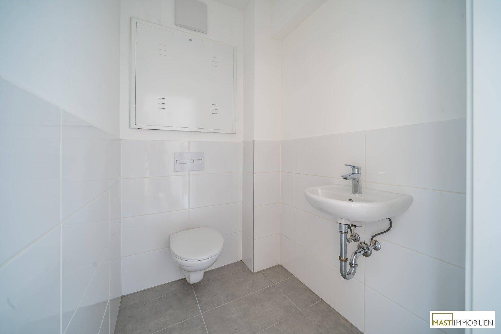 Modernes Gäste-WC mit wandhängender Toilette und kleinem Waschbecken, hell gefliest.
