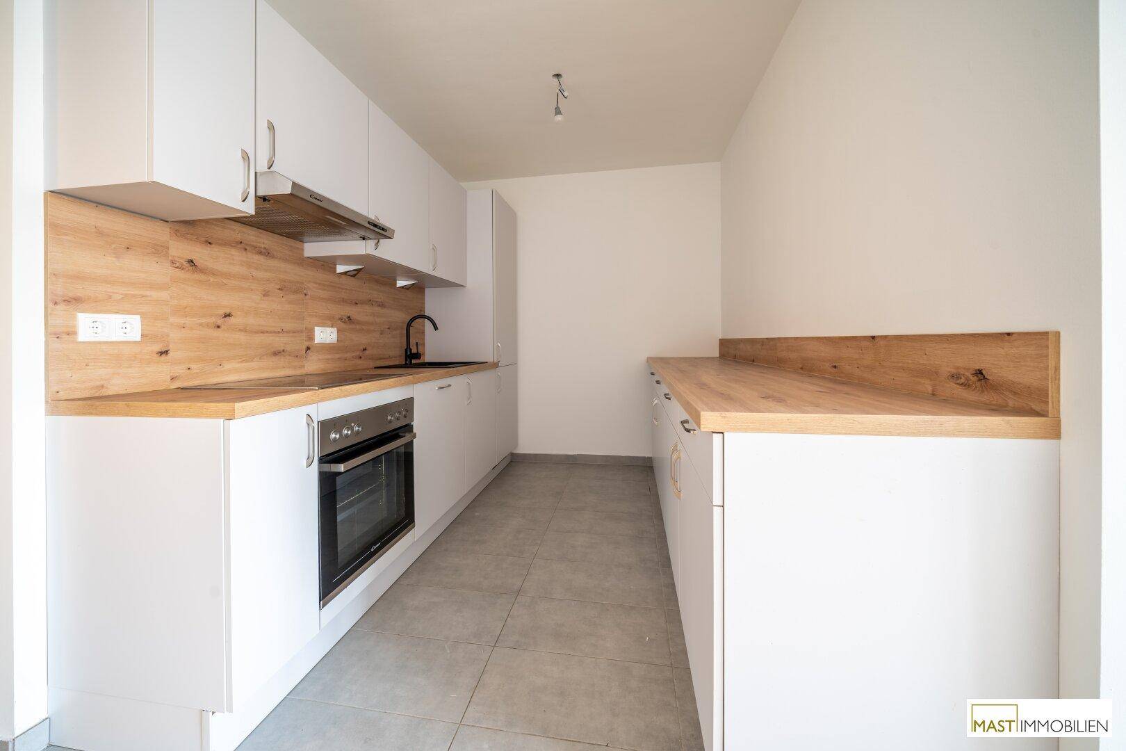 Funktionale Küchenzeile mit weißen Schränken, Holz-Arbeitsplatten und integrierten Elektrogeräten.