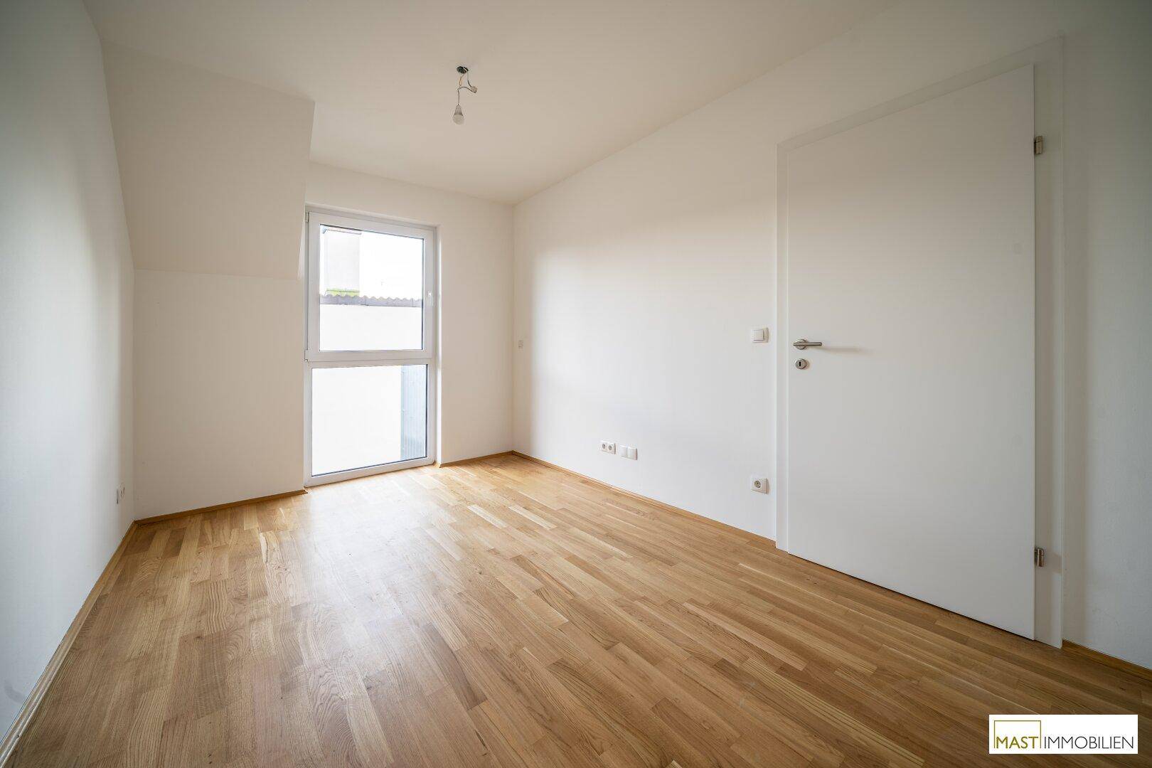 Geräumiges Schlafzimmer mit hellem Parkettboden und einem Fenster für natürliche Belichtung.