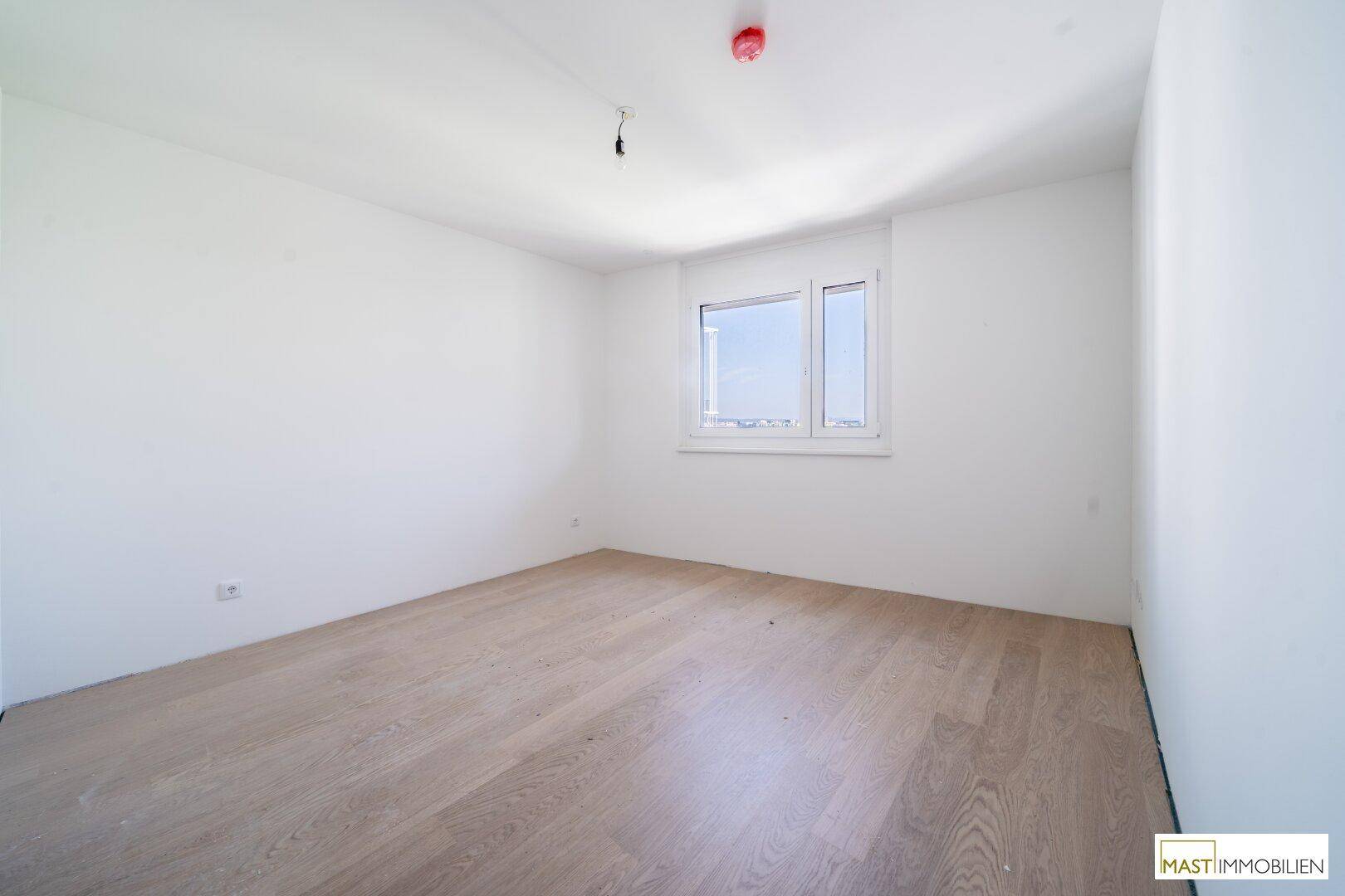 Helles Schlafzimmer mit Parkettboden und einem Fenster, das eine angenehme Atmosphäre schafft.