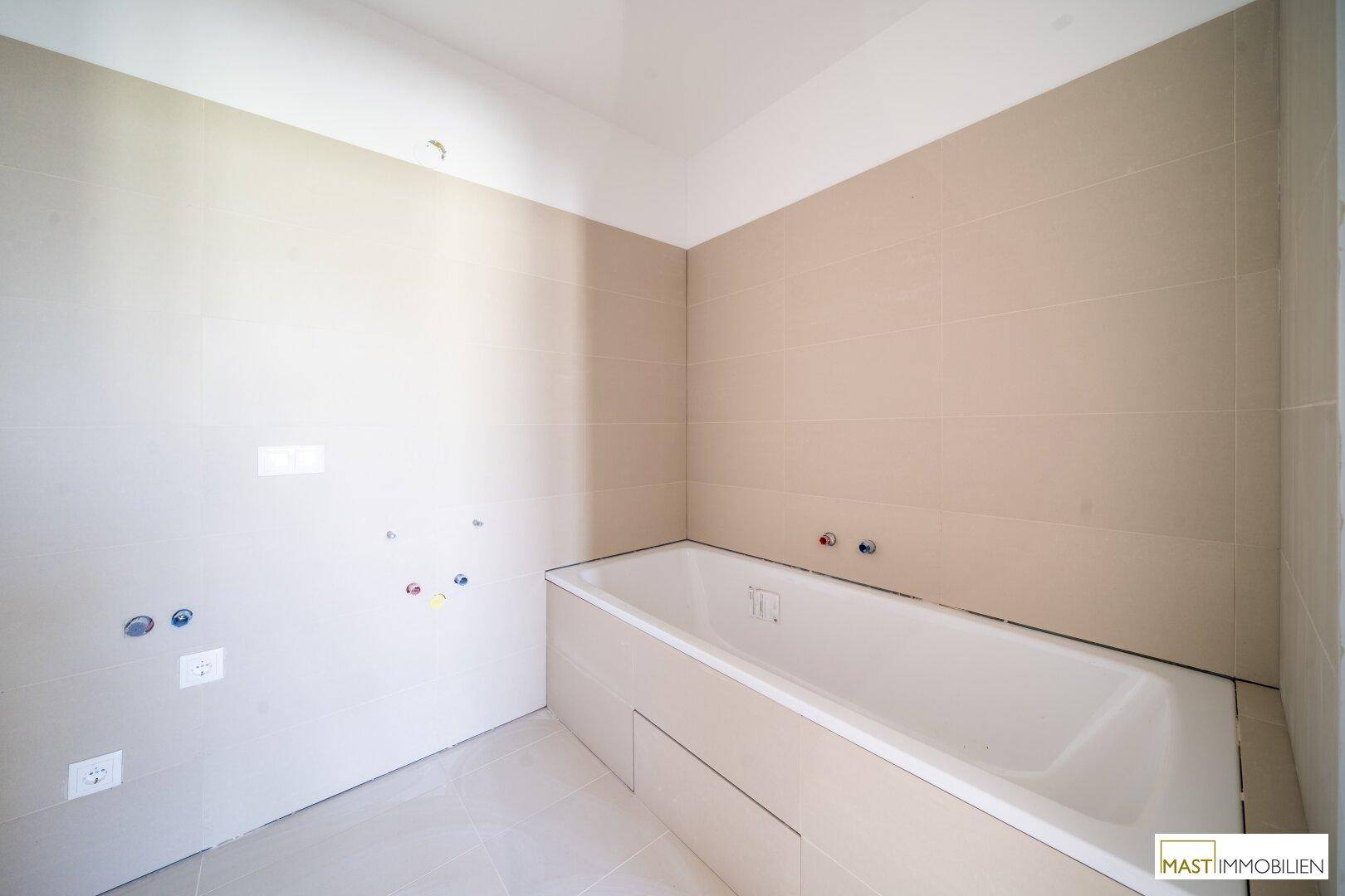 Badezimmer im Bau mit eingebauter Badewanne und beigefarbenen Fliesen an den Wänden, bereit zur Fertigstellung.
