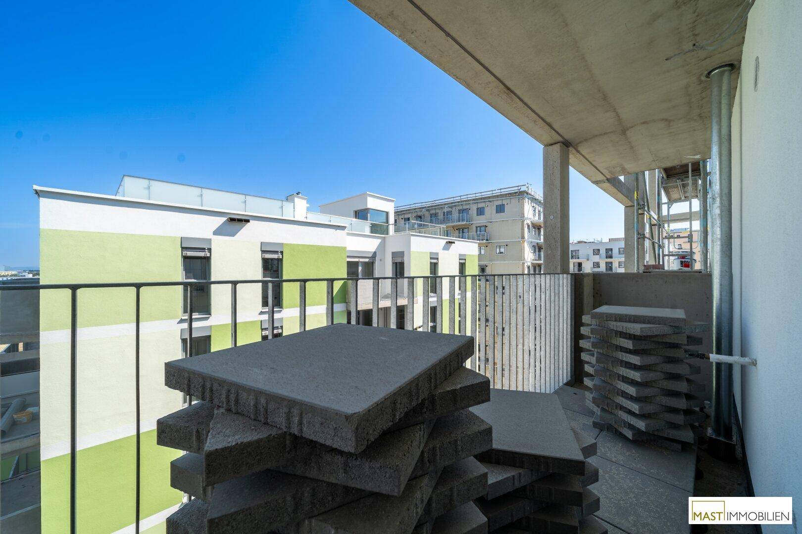 Geräumiger Balkon mit gestapelten Terrassenplatten und freiem Blick auf die Nachbarschaft und den Himmel.