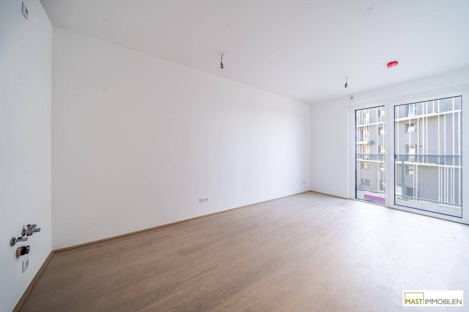 Geräumiges, unmöbliertes Zimmer mit hellem Parkettboden und Anschlussmöglichkeiten an der Wand.