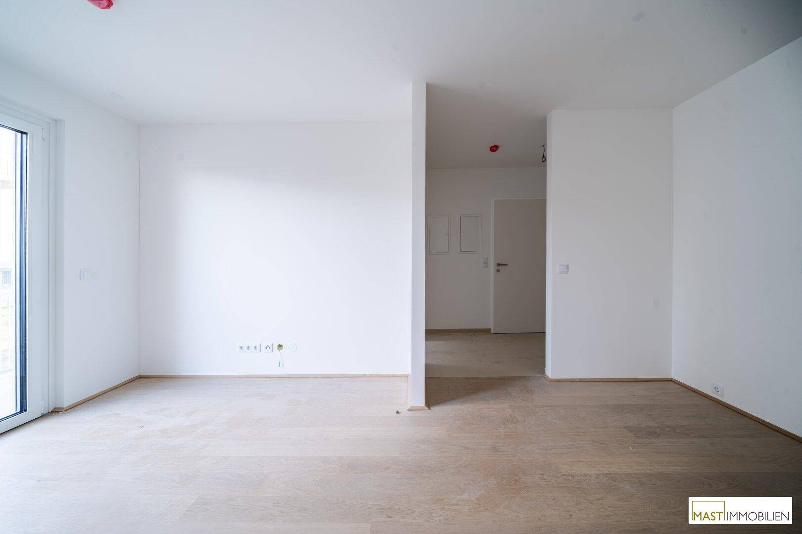 Unmöblierter Raum mit hellem Parkettboden und einer Tür, die zu einem anderen Zimmer führt.